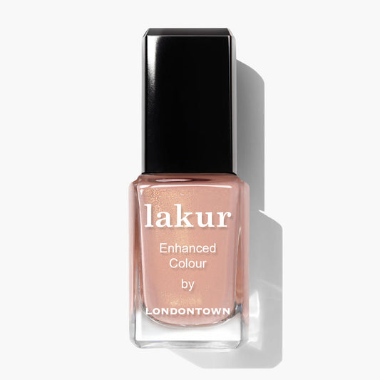 A bottle of LONDONTOWN's Lakur enhanced color nail polish in the shade Amber Lights, featuring a light peachy-pink tone reminiscent of a sunset, set against a plain white background.