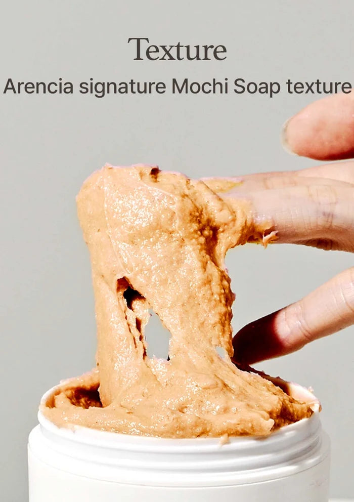 Mochi soap being held with a finger, showing its texture, against a gray background.