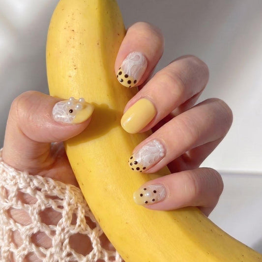 Hand wearing EyeCandys Bananito press on nails featuring bright yellow nails, lace gel detail, and rhinestone accents.