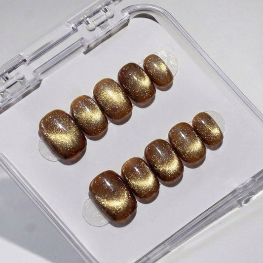 EyeCandys Diet Cola press on nails featuring deep warm brown cat-eye nails with gold micro shimmer and glossy finish in a short round shape.