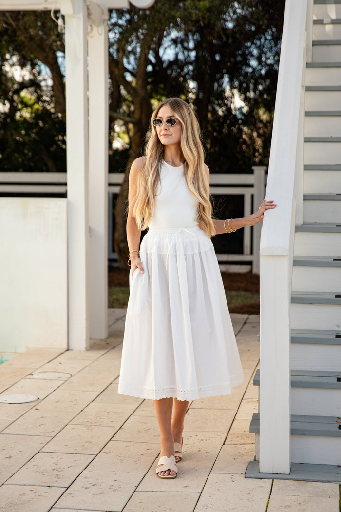 Woman in a white outfit standing on a wooden deck with trees in the background